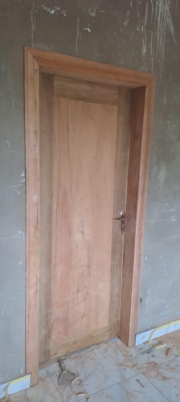 A newly installed smooth wooden door with a matching wooden frame, set against a grey wall and tiled floor.