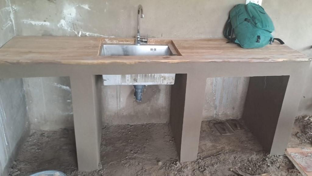 A kitchen counter under construction, showing a teak wood top and a cement base with a metal sink.