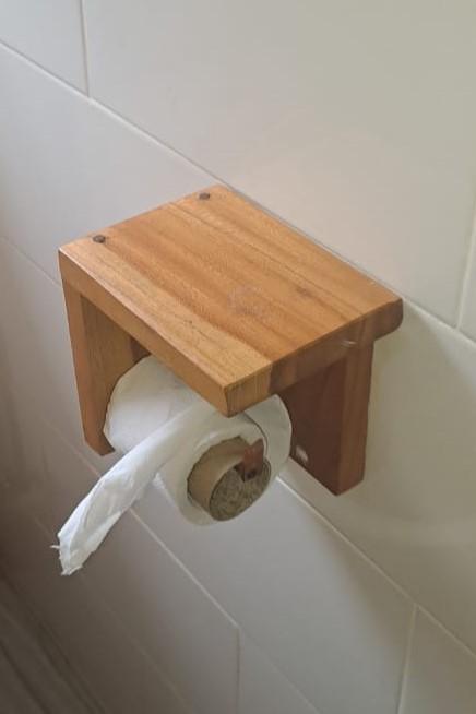A simple, elegant custom-made wooden toilet roll holder mounted on a white tiled wall.